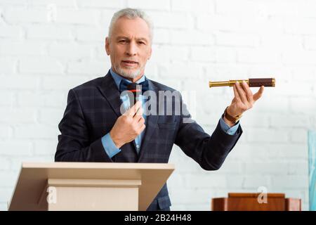 beau encanteur en costume parler avec le microphone et tenir le spyglass pendant la vente aux enchères Banque D'Images