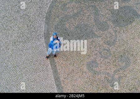 Faro Portugal, 12 décembre 2019 - une jeune fille musulmane sur la place de la vieille ville, prenant des selfies. Vue de dessus, sur l'arrière-plan d'un motif pavé Banque D'Images