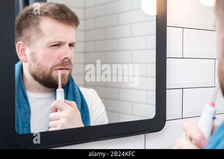 Homme sérieux se brossant les dents avec un irrigateur oral électrique avec un jet d'eau, regardant dans le miroir. Banque D'Images