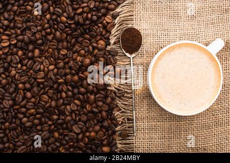 vue de dessus des grains de café fraîchement torréfiés et des sackcloth avec cappuccino et cuillère avec café moulu Banque D'Images