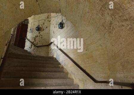 Escalier en colimaçon dans un vieux bâtiment en pierre délabrée avec un plafond voûté. Rampes et lampes modernes Banque D'Images