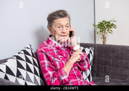 Vieux thème personne utilise la technologie. Happy mature joie sourire cheveux gris active Caucasian woman rides accueil dans le salon sur le canapé et à l'aide d'un Banque D'Images