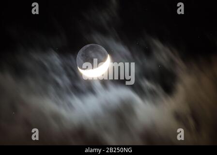 Une lune de croissant est encadrée par des nuages qui passent rapidement tandis que les étoiles brillent dans un ciel noir au-delà. Banque D'Images