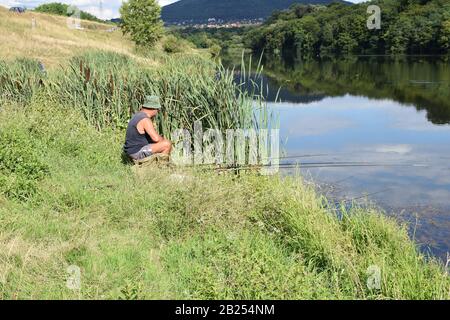 Sur une rive verte dans l'herbe haute, un homme est assis et poisson Banque D'Images