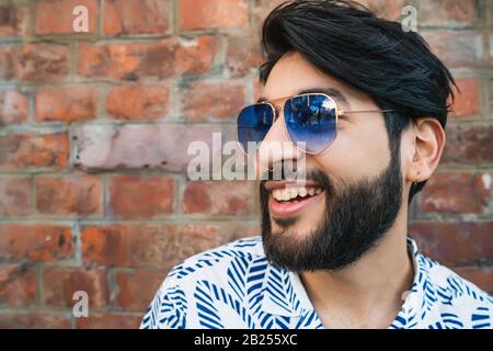 Portrait de jeune homme séduisant portant des vêtements d'été et lunettes contre mur de briques. Concept urbain. Banque D'Images