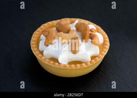 Tartelettes sucrées au citron, aux noix et à la crème protéique. Gâteau avec crème fouettée et base de pâte à croûte courte. Gâteau rond avec noix de cajou sur un dos noir Banque D'Images