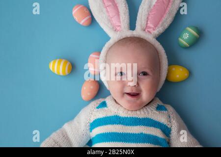 Joli bébé portant des oreilles de lapin de pâques entourées d'œufs de pâques. Banque D'Images