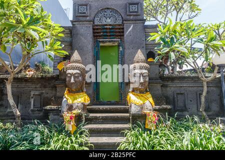 Statues en pierre de deux têtes de Bouddha décorées dans un tissu 'prada' doré près d'une maison balinaise traditionnelle à Desa Munggu, Bali, Indonésie. Banque D'Images