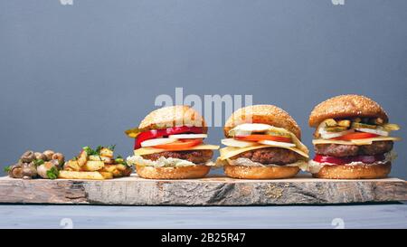hamburgers juteux avec pommes de terre et champignons frits sur une plaque en bois. hamburgers avec fromage et légumes sur fond gris. Banque D'Images