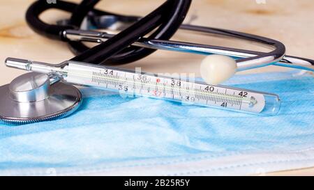 Thermomètre à statoscope et masque médical jetable sur le visage de près. Protection contre les maladies virales et bactériennes grippe froide COVID-19 rougeole. Banque D'Images