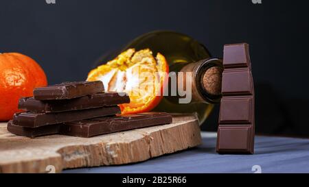 morceaux de chocolat, de tangerines et une bouteille de vin sur une plaque de bois. ingrédients de vin chaud. Banque D'Images