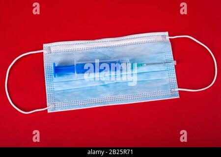 Précautions pour l'infection virale du coronavirus, covid-2019. Masque de protection médicale bleu et seringue avec vaccin sur fond rouge. Banque D'Images