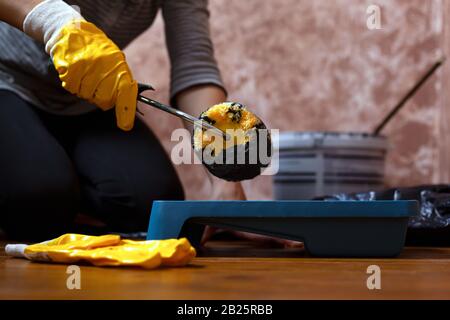 maître en gants de travail jaunes maintient le rouleau sur le plateau avec de la peinture grise. préparation pour la peinture des murs et des plafonds. outils de réparation. Banque D'Images