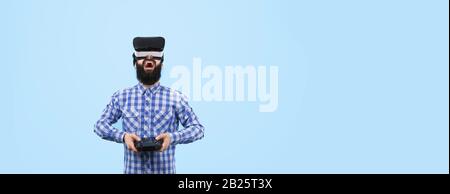 Homme barbu surpris en VR (lunettes de réalité virtuelle) avec télécommande à la main contrôle la drone, image sur fond bleu, maquette panoramique avec Banque D'Images