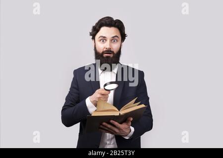 un livre de lecture barbu choqué avec loupe, homme sur fond gris Banque D'Images