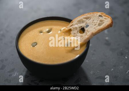 Soupe à la crème de citrouille avec graines de citrouille et crouton de baguette dans un bol noir sur fond de béton, peu profond foyer Banque D'Images