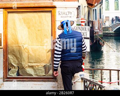 Gondolier à Venise offrant le service de transport (sur le mur est peint le nom du célèbre pont du Rialto avec une indication pour la directio Banque D'Images