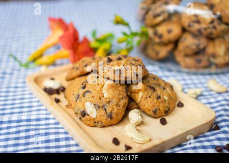 gros plan de cookies aux pépites de chocolat et aux noix, décorés sur une plaque en bois avec un bocal à biscuits et des fleurs sur un tissu de table à carreaux bleu et blanc Banque D'Images