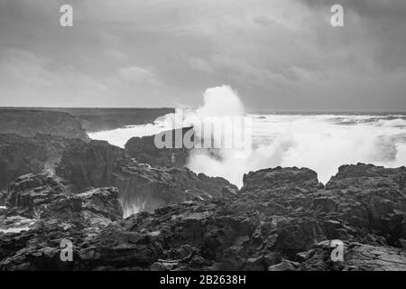 Brimketill piscine de roche de lave Islande énorme vague frappant la côte noire de basalte en noir et blanc Banque D'Images