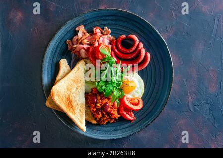 Vue sur le dessus de l'oeuf frit, de la saucisse, du bacon, des légumes et du pain grillé Banque D'Images