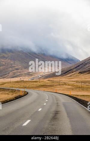 Nord de l'Islande route vide se serpentant dans la vallée vers le haut d'une montagne par temps gris désagréable Banque D'Images