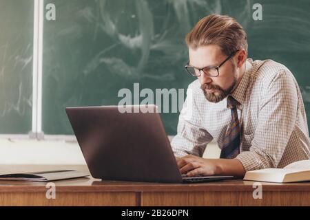 Professeur barbu concentré dans des lunettes utilisant un ordinateur portable pendant les conférences de pause Banque D'Images