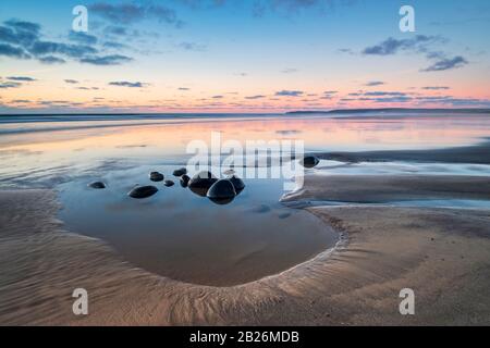 Des cailloux dans une piscine en pierre sur Westward Ho! Plage, North Devon avec coucher de soleil à l'horizon Banque D'Images