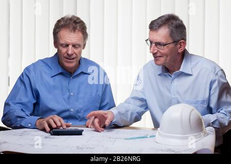 Deux architectes ou ingénieurs matures qui ont calcuté un projet à un bureau avec plan directeur Banque D'Images