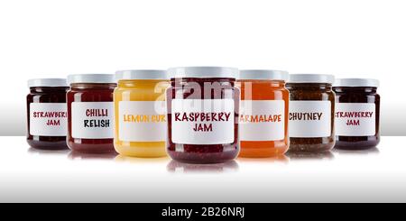 Un bocaux de groupe contenant des confitures et des conserves, y compris la rasperry, la fraise, la marmalade, le chutney et le relish, sur une table blanche comme la surface, avec un blanc Banque D'Images