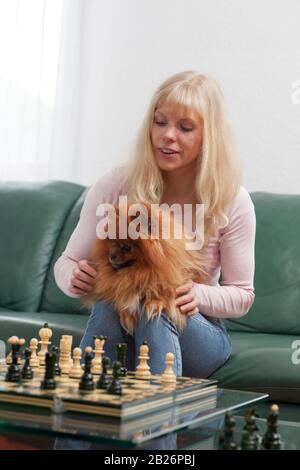 Jolie jeune femme souriante jouant aux échecs avec son animal dans ses bras dans un salon lumineux Banque D'Images