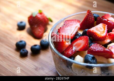 Céréales dans un bol en verre avec banane, fraises, bleuets et miel sur la table en bois. Banque D'Images