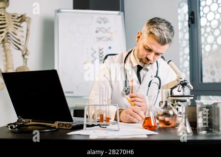 Homme principal, chercheur scientifique écrit des notes, observations de laboratoire. Chercheur masculin effectuant des recherches scientifiques, assis à la table, test Banque D'Images