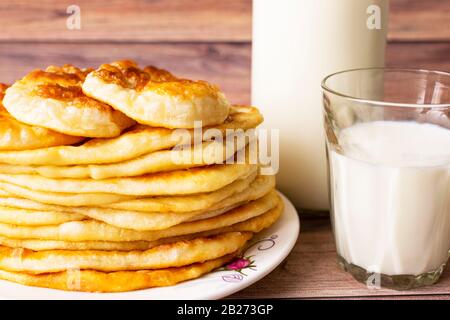 Nourriture saine et rustique. Du lait dans une bouteille, un verre et des gâteaux chauds pour le petit-déjeuner. Blé, gâteaux de farine de maïs. Fond en bois Banque D'Images