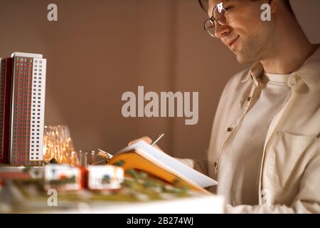 sourire heureux homme pensant à sa petite amie tout en travaillant sur le projet, gros plan photo vue latérale. architecte rêve de construire original, parfait, crea Banque D'Images