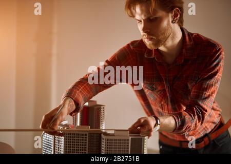 Professionnel gingembre sérieux architecte travaillant au bureau, il fait des mesures d'un modèle, design et architecture concept. Gros plan photo. Banque D'Images