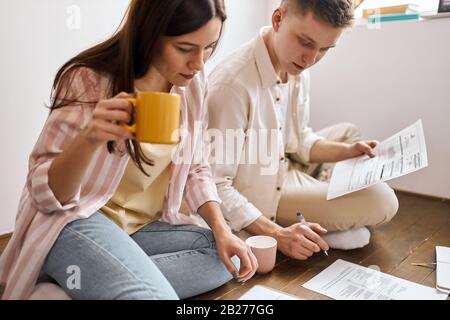 un jeune couple a concentrique avec des doculants, des factures de contrôle, une photo rapprochée. une femme sérieuse tenant une tasse de café et regardant le papier Banque D'Images