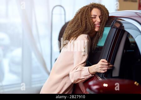 Jeune fille émotionnelle embrassant sa nouvelle voiture, je t'aime, vous êtes mon bébé, fort sentiment, dame qui collecte des voitures modernes. Gros plan photo Banque D'Images