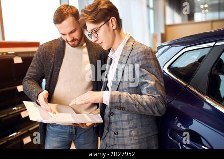 jeune assistant de magasin élégant et homme lisant les caractéristiques, conditions de contrat. gros plan photo vue latérale. homme et client regardant le papier, aaliz Banque D'Images