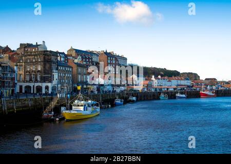 Bateau de plaisance jaune et bateaux de pêche bleus et rouges attachés au quai à poissons dans le port de Whitby North Yorkshire. Banque D'Images