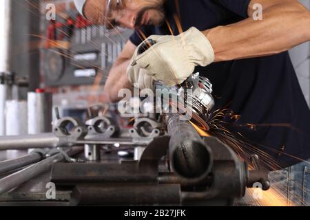 L'homme travail dans l'atelier de maison avec garage, meuleuse d'angle et de la construction des lunettes, gants de métal ponçage rend gros plan sparks, bricolage et artisanat concept Banque D'Images