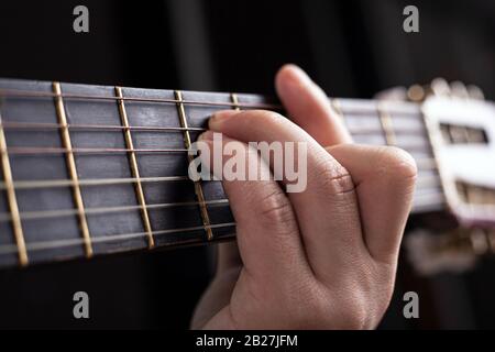 la main mâle serre une corde de guitare acoustique. apprendre à jouer l'instrument de gros plan. Banque D'Images