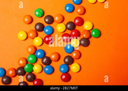 repas de vacances chocolat multicolore petits bonbons dispersés sur un fond orange vue de dessus de gros plan. Banque D'Images