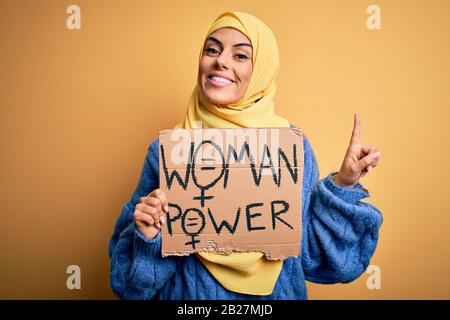 Jeune femme arabe portant une bannière islamique hijab tenant des femmes message de pouvoir surpris par une idée ou une question pointant doigt avec heureux Banque D'Images