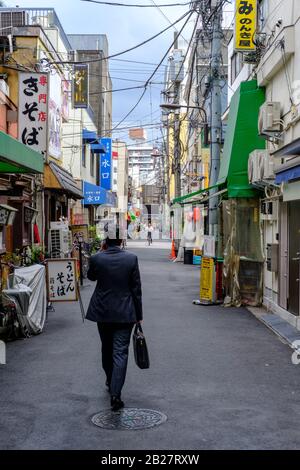 Un homme d'affaires traverse une petite rue typique de Tokyo, au Japon, en été 2019. Banque D'Images