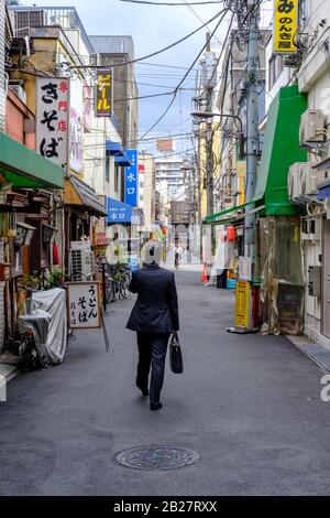 Un homme d'affaires traverse une petite rue typique de Tokyo, au Japon, en été 2019. Banque D'Images