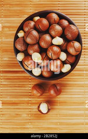 Noix de macadamia sur la texture du bambou dans une tasse en bois, noyer pelé et non pelé, vue de dessus Banque D'Images