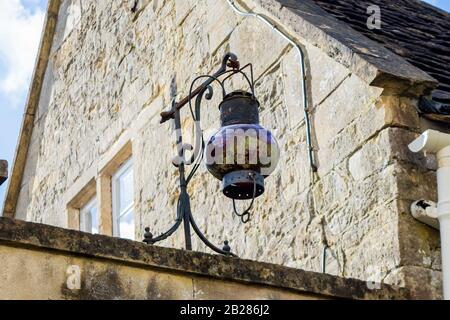 Une lampe à huile ancienne convertie en métal électrique et un globe en verre rouge bien patiné avec une suspension verte d'un support d'un mur à côté d'un ho Banque D'Images