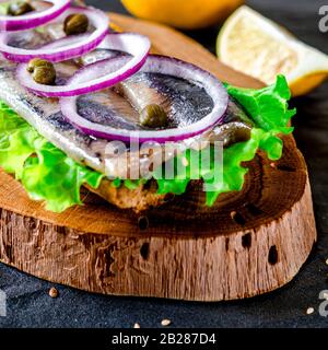 Le smorrebrod appétissant avec le hareng norvégien, la laitue, l'oignon bleu, le citron et la tomate se trouve sur une planche en bois Banque D'Images