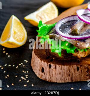 Le smorrebrod appétissant avec le hareng norvégien, la laitue, l'oignon bleu, le citron et la tomate se trouve sur une planche en bois Banque D'Images