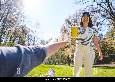 homme posé sur un canapé-lit dans un parc public femme allant et tenant une tasse de papier avec thé Banque D'Images